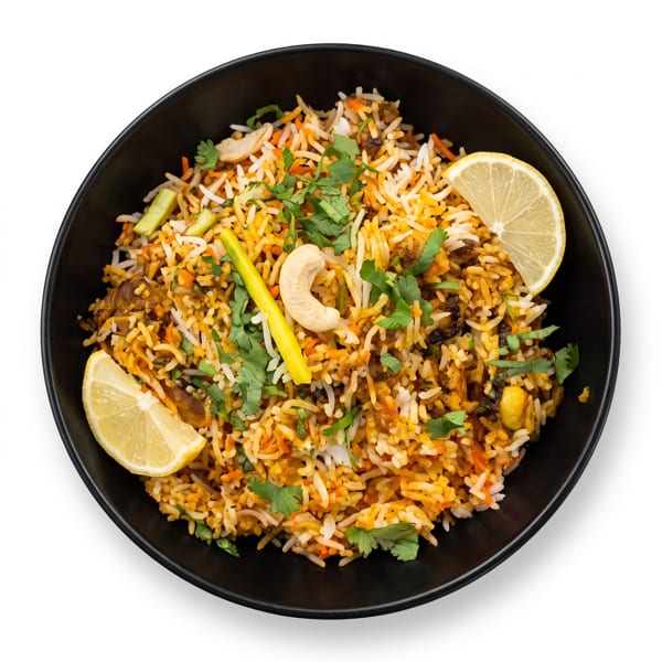Overhead view of a black bowl filled with colorful biryani, garnished with lemon, cashews, and cilantro.