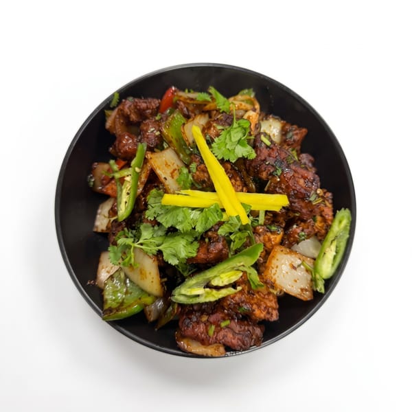 Spicy chicken dish with green peppers, onions, and cilantro in a black bowl.