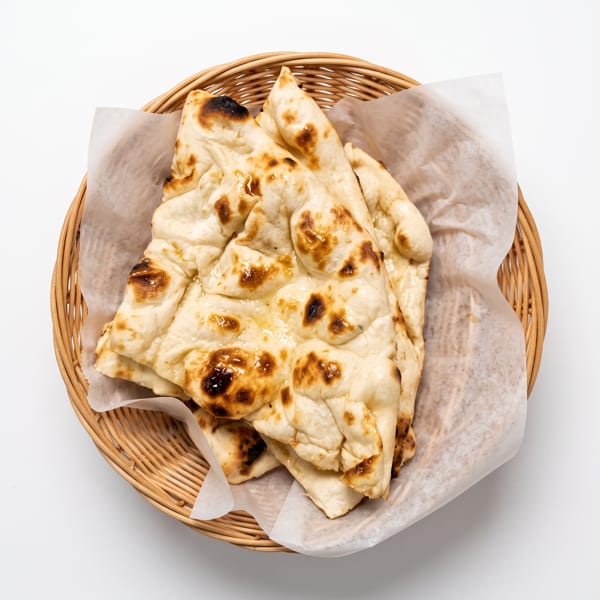 Golden-brown naan bread, lightly charred, served in a woven basket lined with white paper.
