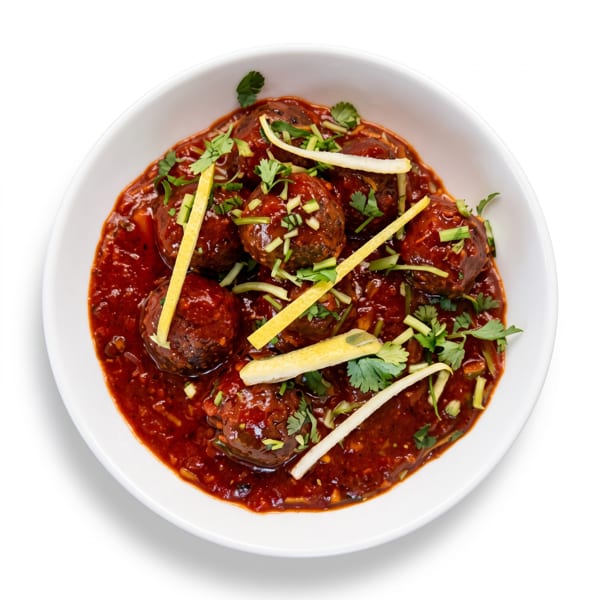 A white bowl filled with dark red meatballs in sauce, garnished with cilantro and lemon strips.