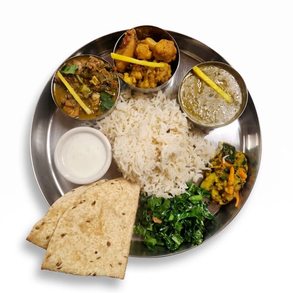 A Nepali thali meal with rice, curries, flatbread, and vegetables on a metal plate.